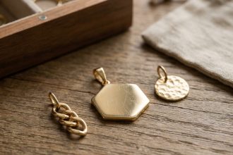 Trois pendentifs en or unisexes posés sur bois, incluant un hexagone géométrique, un design chaîne et un disque martelé
